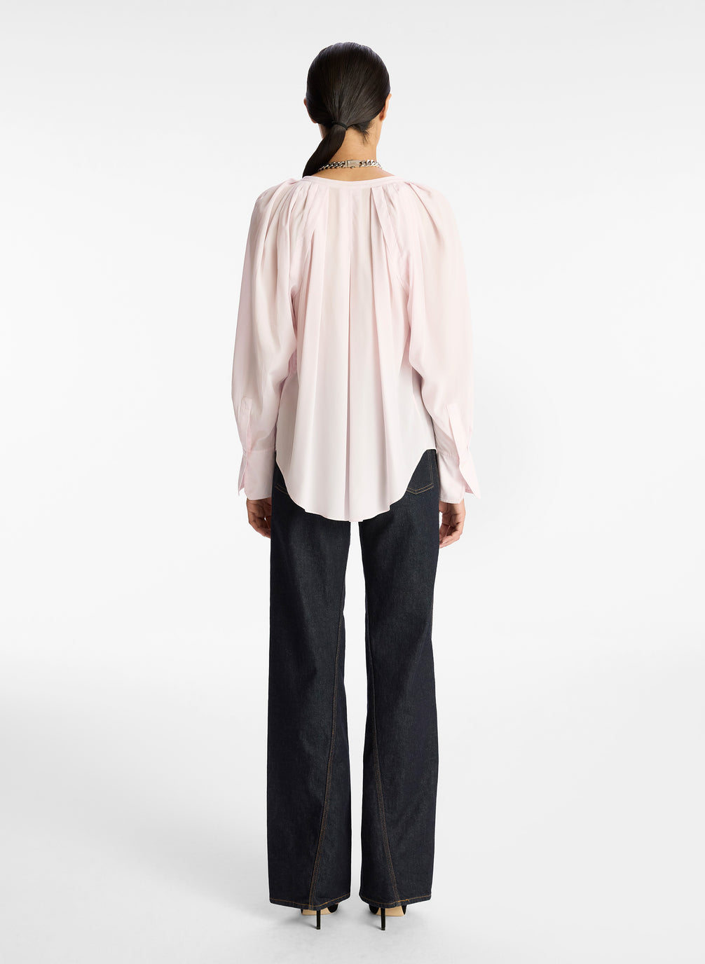 back view of woman wearing light pink v neck long sleeve silk top and dark wash denim jeans