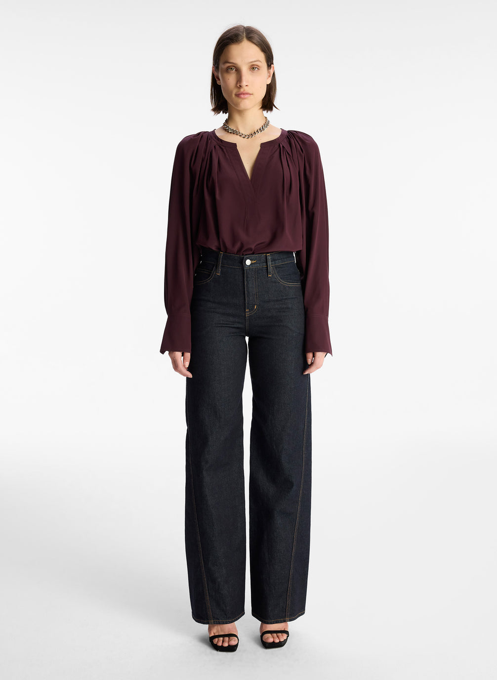front view of woman wearing burgundy v neck long sleeve silk top and dark wash denim jeans