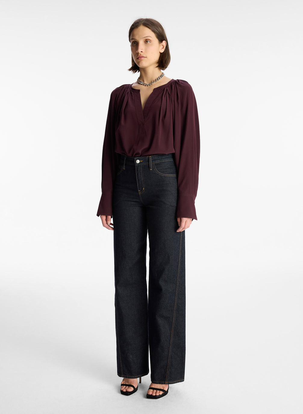 side view of woman wearing burgundy v neck long sleeve silk top and dark wash denim jeans