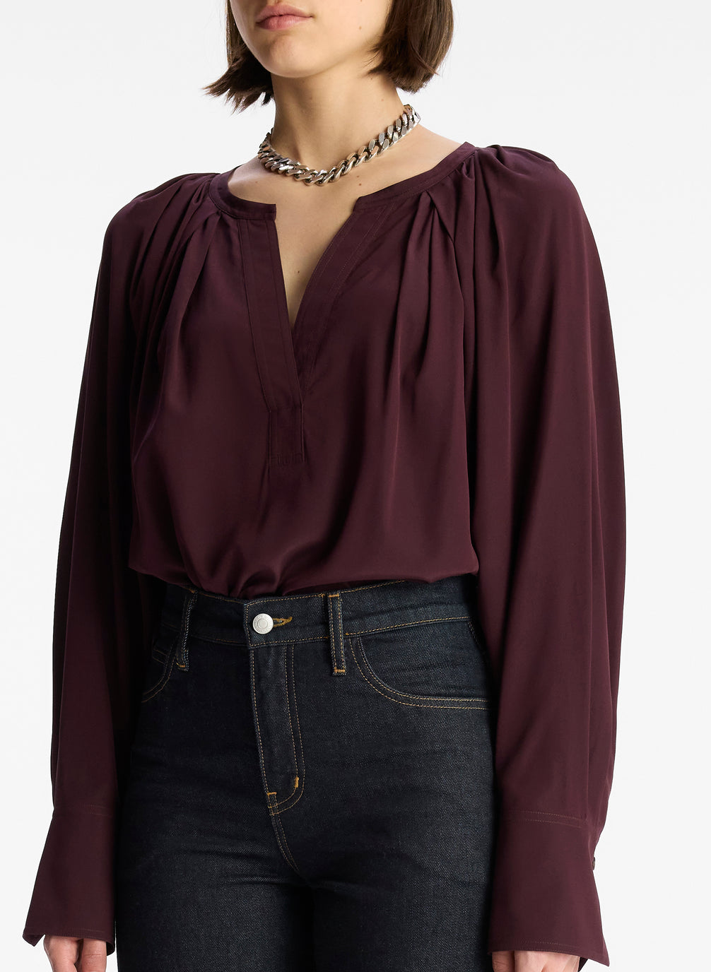 detail view of woman wearing burgundy v neck long sleeve silk top and dark wash denim jeans