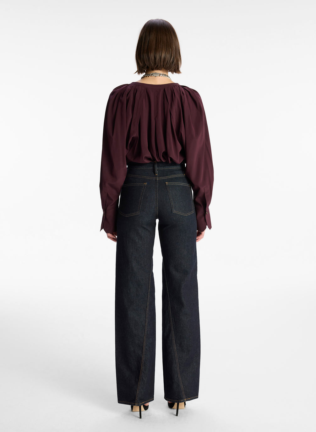 back view of woman wearing burgundy v neck long sleeve silk top and dark wash denim jeans