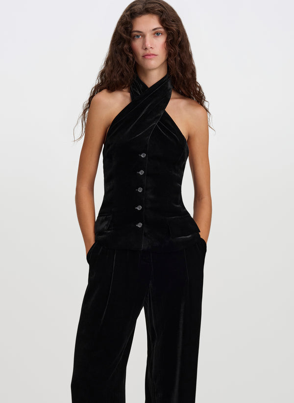 A model wearing a black velvet one-shoulder halter top with a button-front detail and matching wide-leg trousers, photographed against a plain light gray studio background.