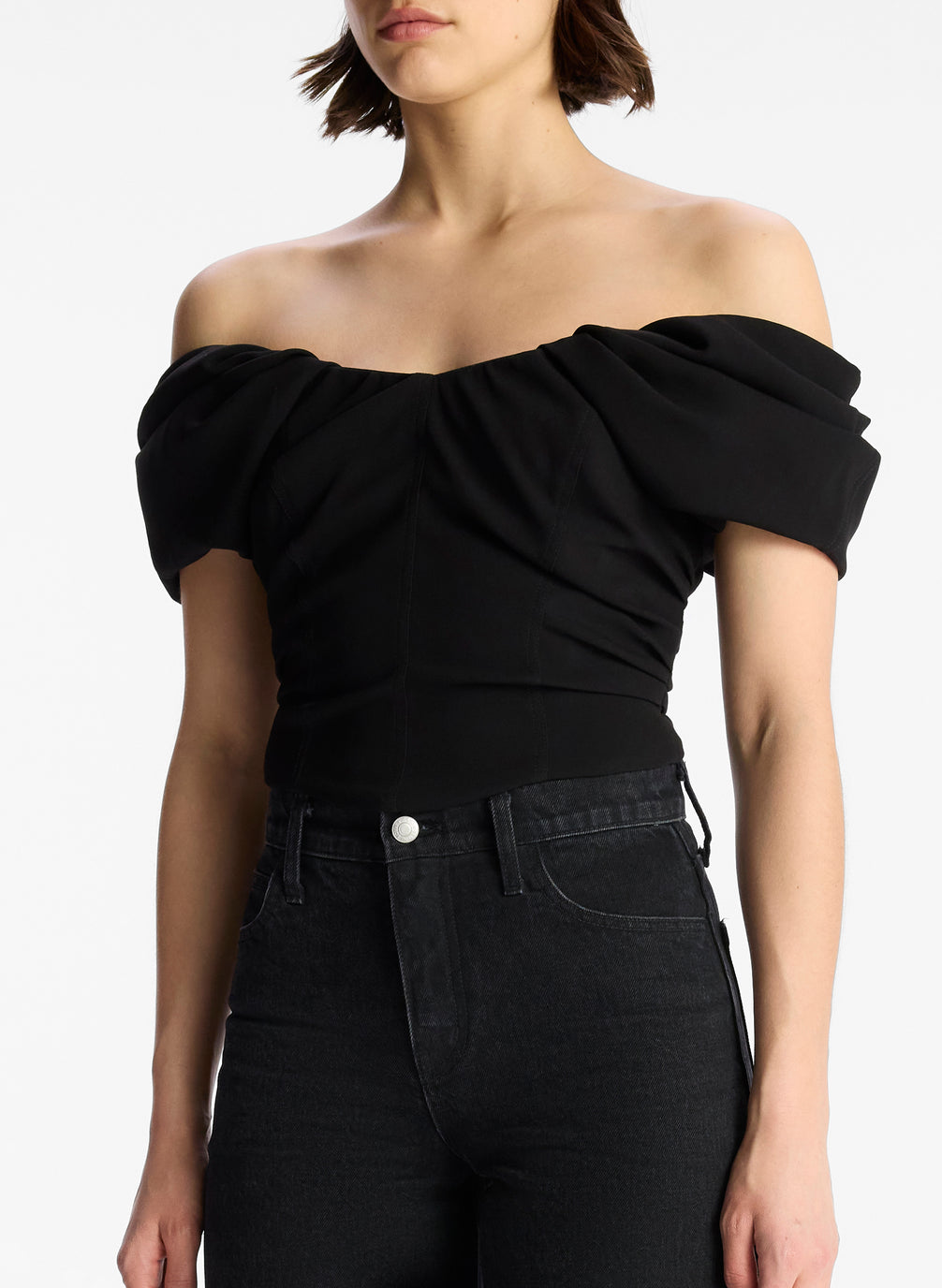 detail view of woman wearing black off shoulder puff sleeve top and dark wash denim jeans