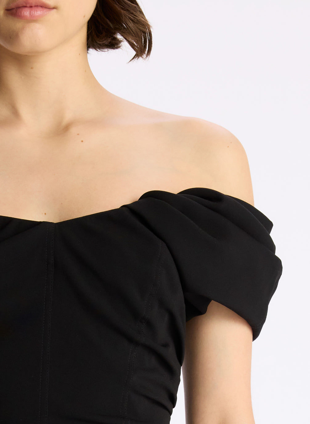detail view of woman wearing black off shoulder puff sleeve top and dark wash denim jeans