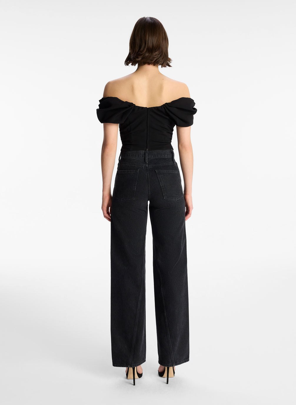 back view of woman wearing black off shoulder puff sleeve top and dark wash denim jeans