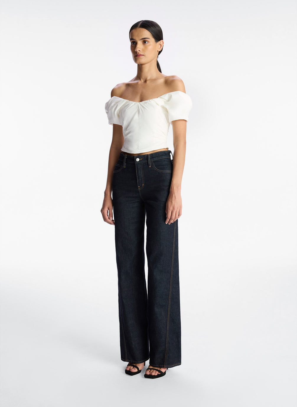 side view of woman wearing white off shoulder puff sleeve top and dark wash denim jeans