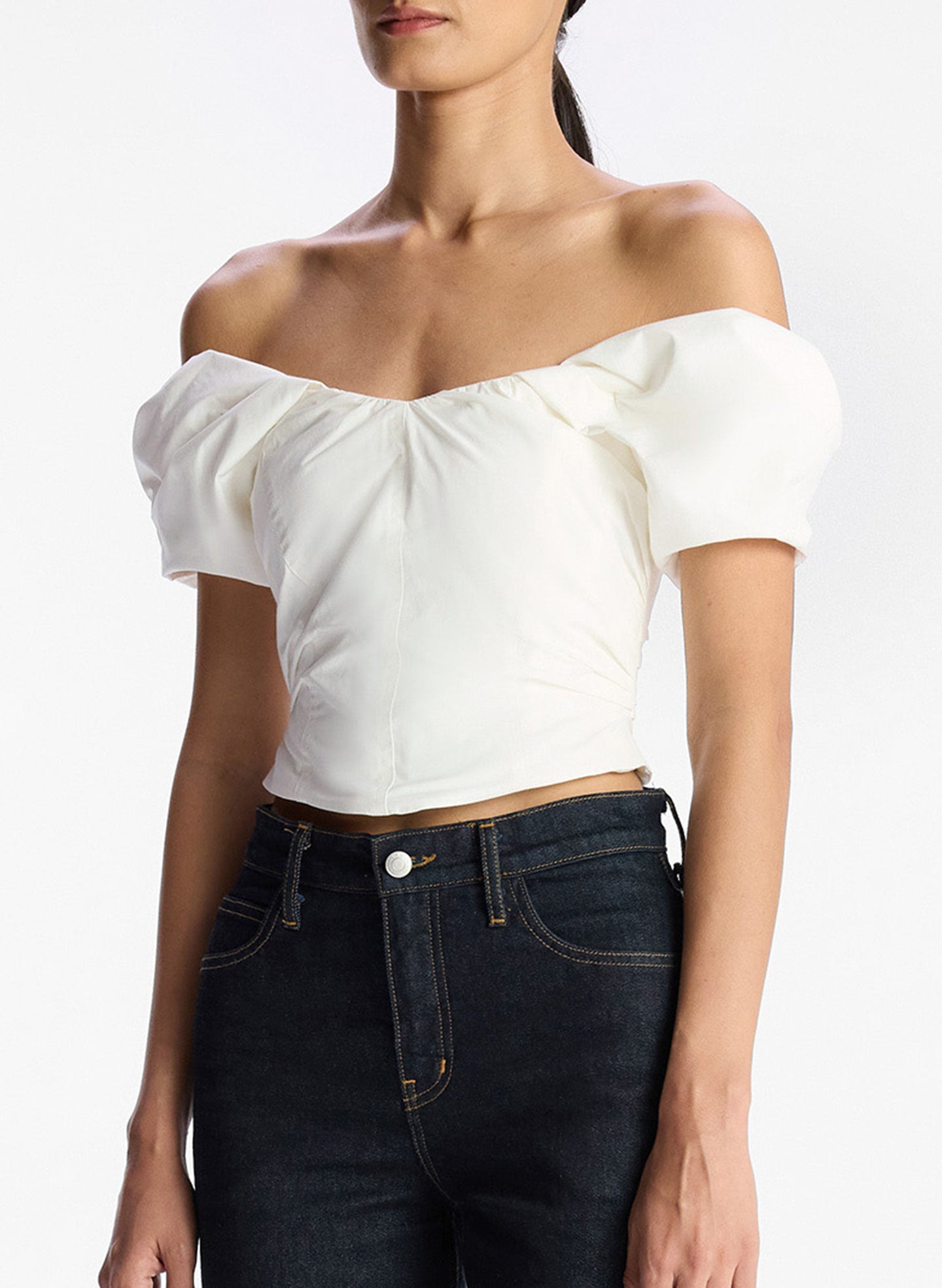 detail view of woman wearing white off shoulder puff sleeve top and dark wash denim jeans