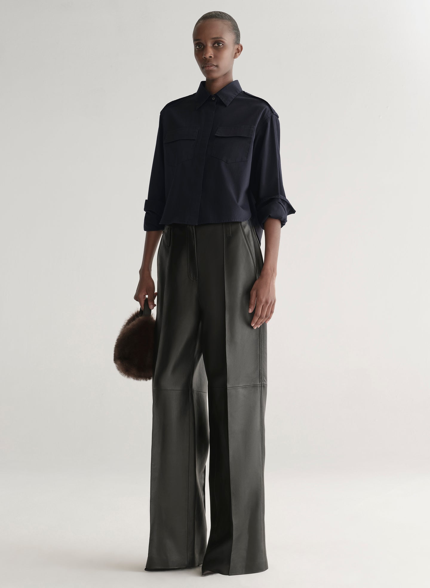 woman wearing a dark navy blue shirt and black leather pants against a plain background