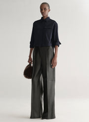 woman wearing a dark navy blue shirt and black leather pants against a plain background