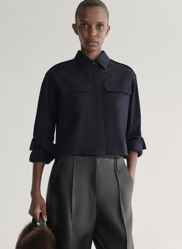 woman wearing a dark navy blue shirt and black leather pants against a plain background