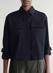 woman wearing a dark navy blue shirt and black leather pants against a plain background