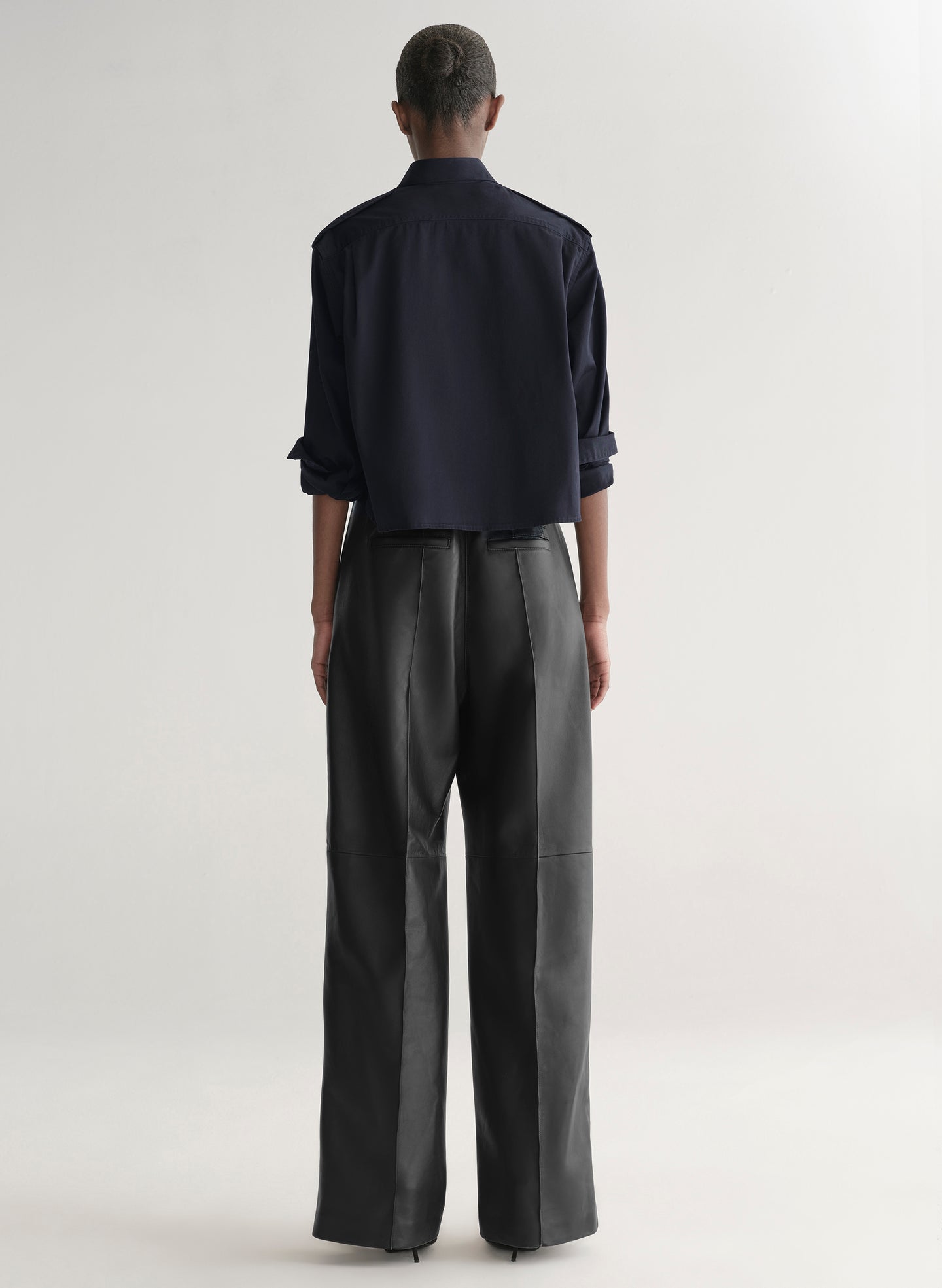 woman wearing a dark navy blue shirt and black leather pants against a plain background