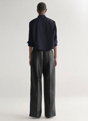 woman wearing a dark navy blue shirt and black leather pants against a plain background