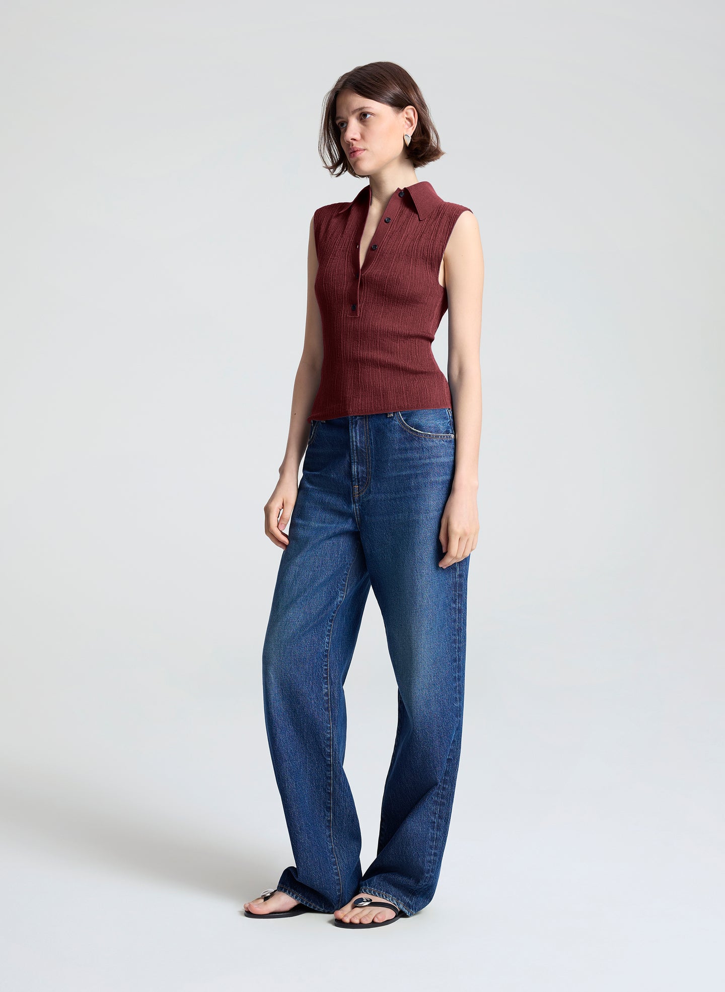 woman wearing burgundy sleeveless polo top and wide leg dark blue denim jeans