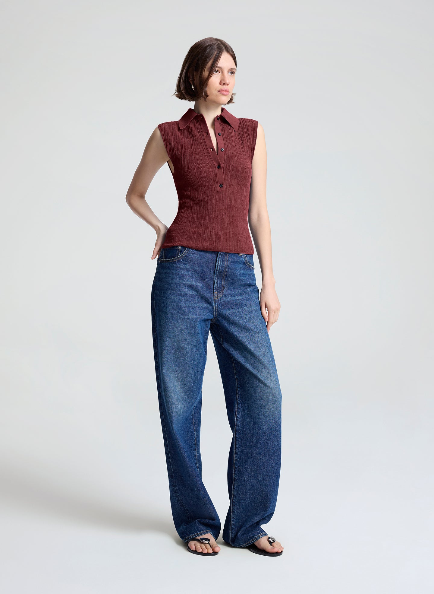woman wearing burgundy sleeveless polo top and wide leg dark blue denim jeans