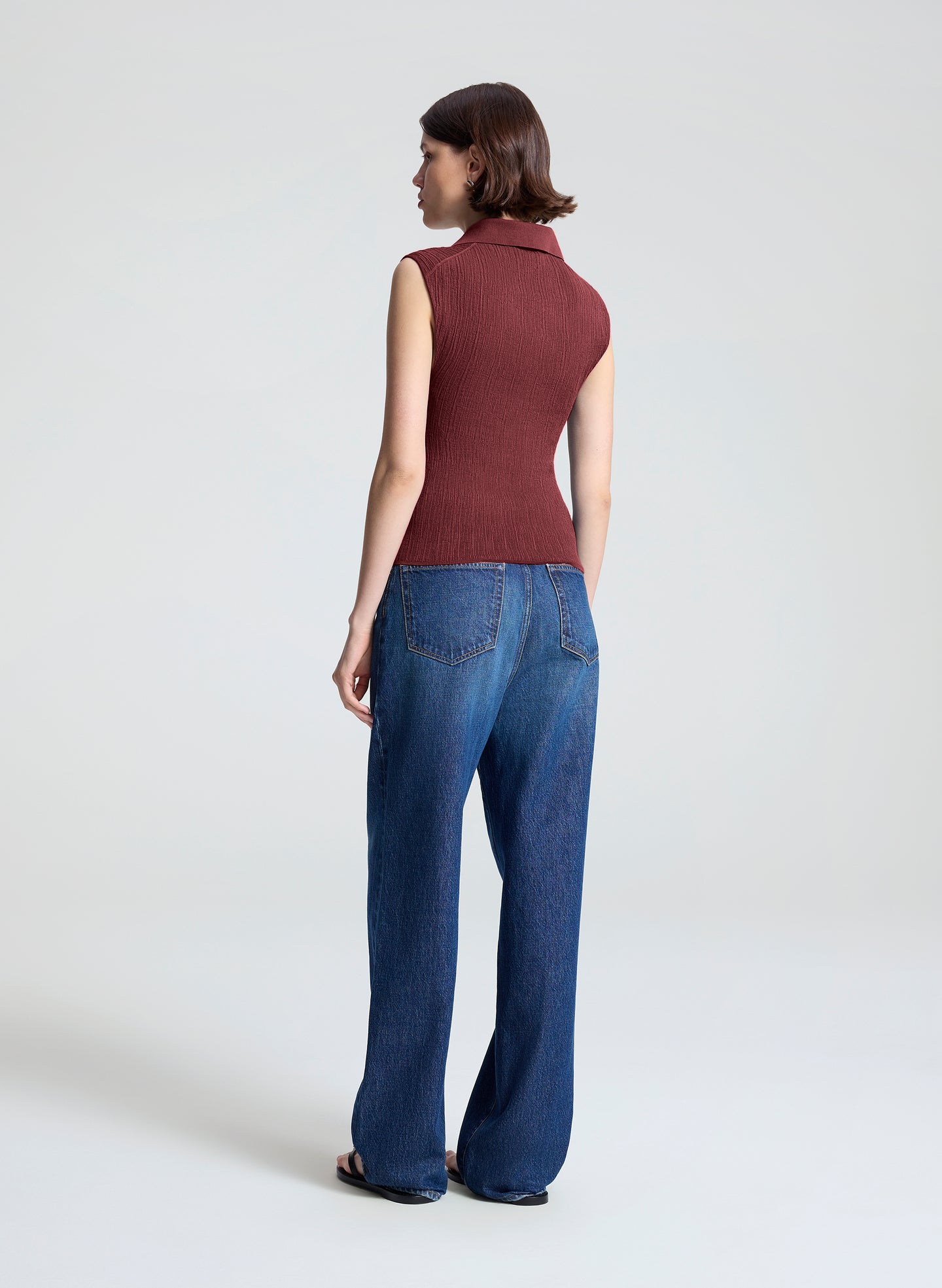 woman wearing burgundy sleeveless polo top and wide leg dark blue denim jeans