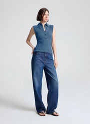 A woman modeling a sleeveless blue button-front top and wide-leg blue jeans against a plain light gray studio background.