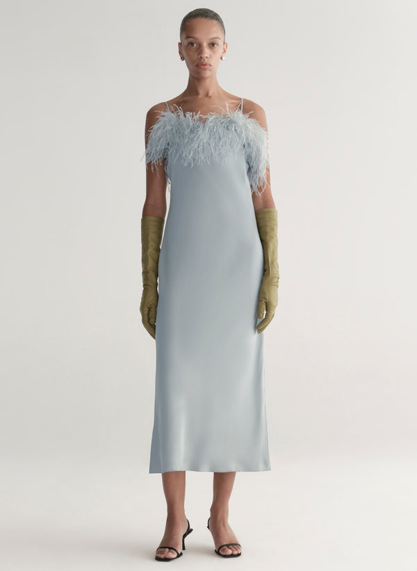 Woman wearing a light blue off-shoulder dress with feather details and green gloves on a white background