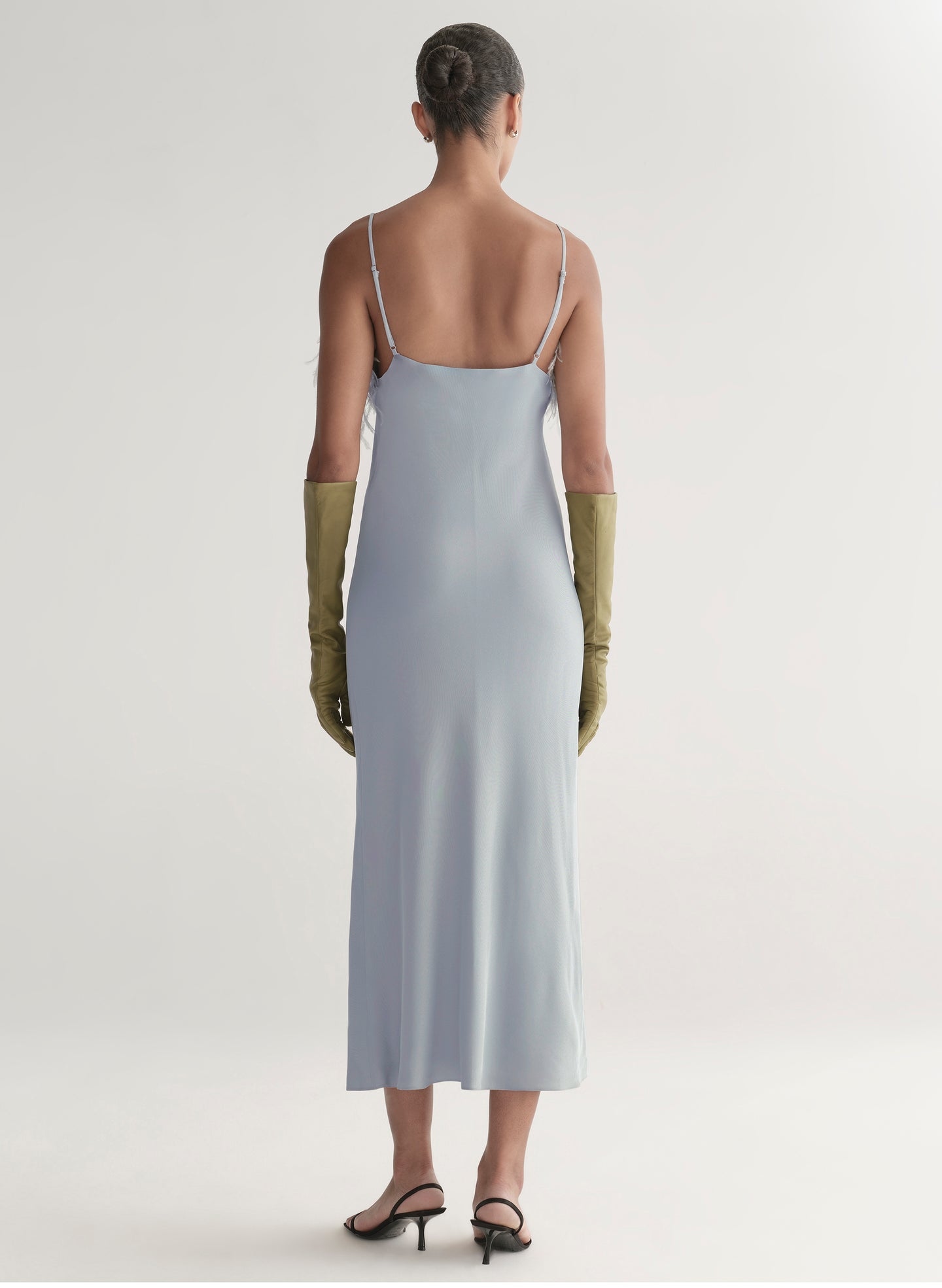 Woman wearing a light blue slip dress with thin straps and green gloves on a white background