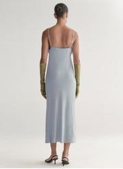 Woman wearing a light blue slip dress with thin straps and green gloves on a white background