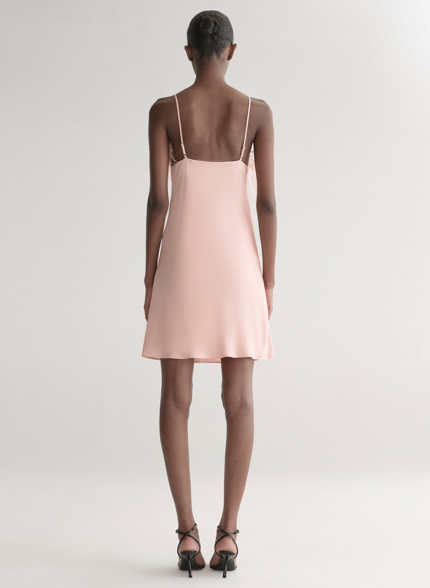 Woman wearing a light pink dress with feather details on a white background