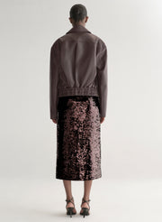 Woman wearing a maroon leather jacket and sequin skirt on a plain background