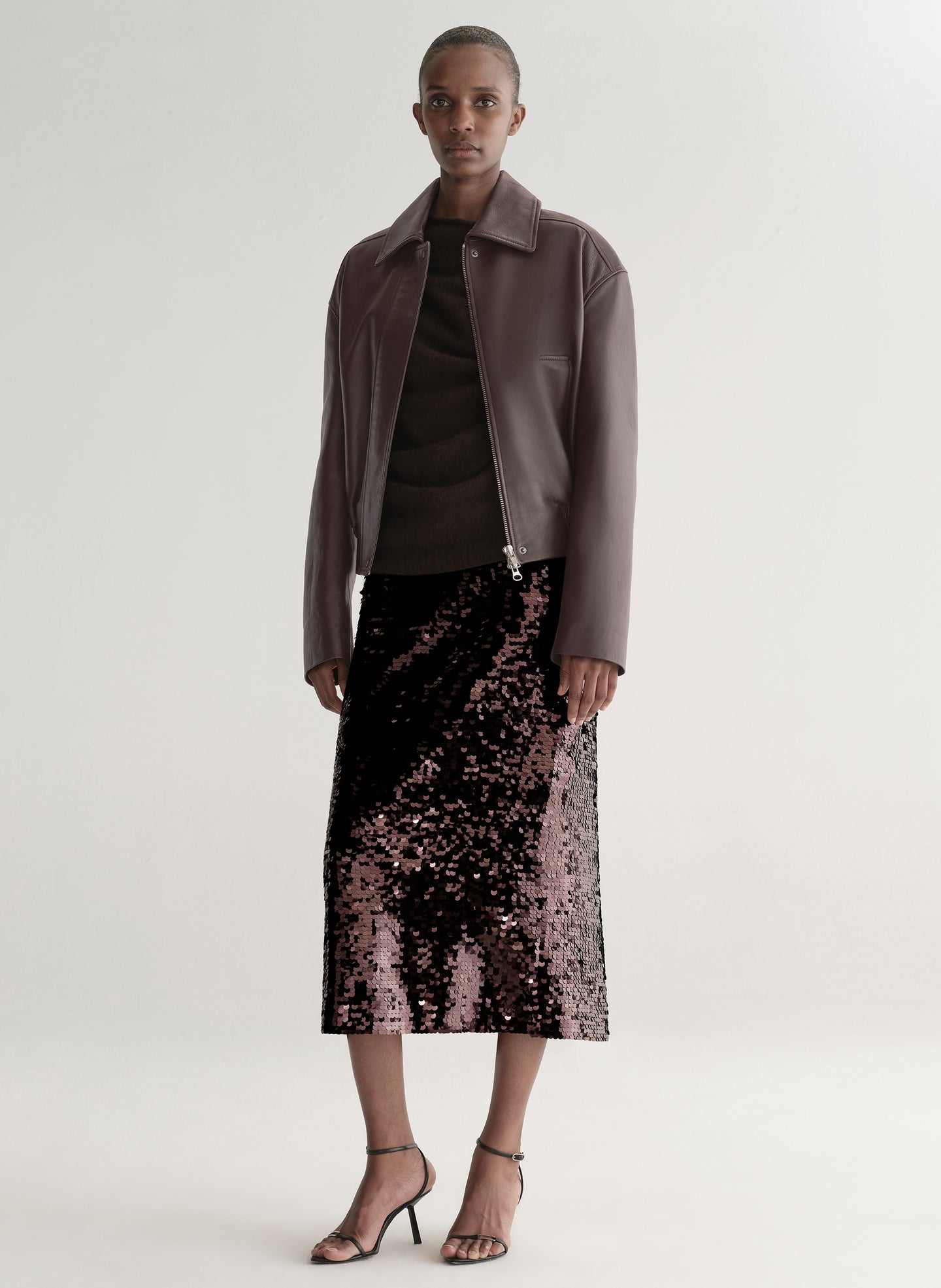 Woman wearing a maroon leather jacket and sequin skirt on a plain background