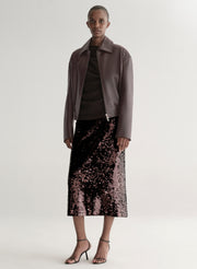 Woman wearing a maroon leather jacket and sequin skirt on a plain background