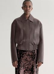 Woman wearing a maroon leather jacket and sequin skirt on a plain background