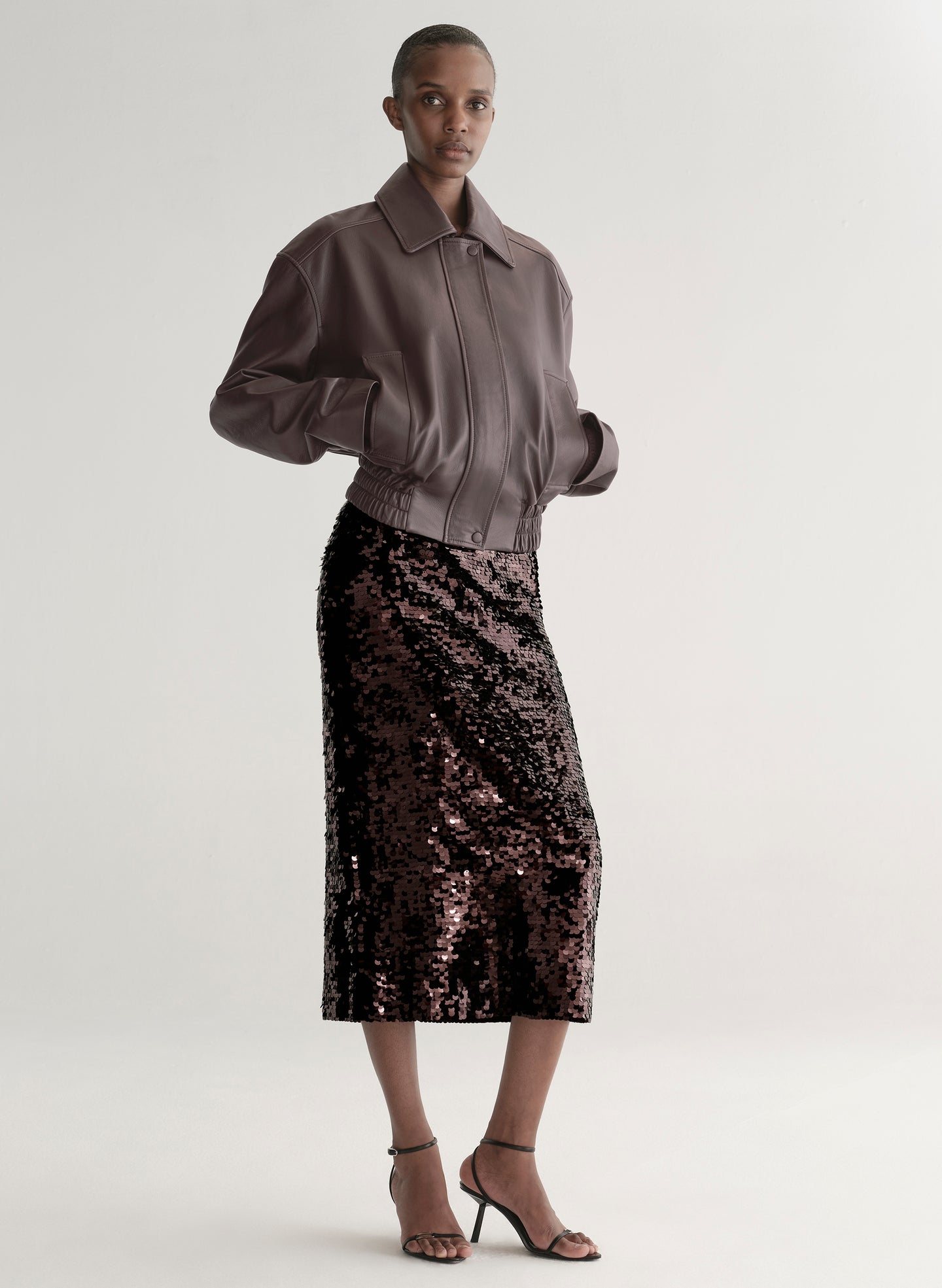 Woman wearing a maroon leather jacket and sequin skirt on a plain background