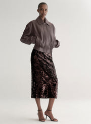 Woman wearing a maroon leather jacket and sequin skirt on a plain background