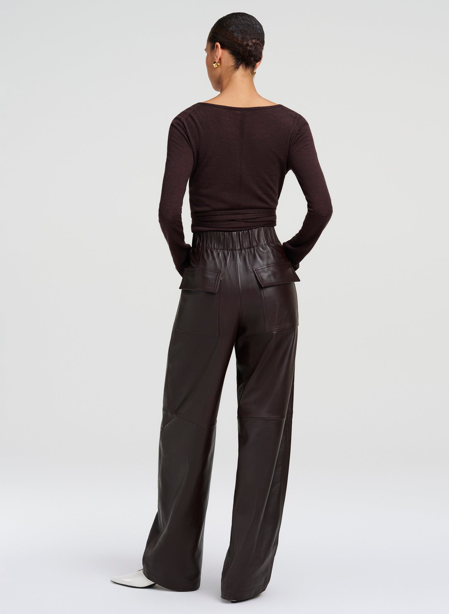 A model shown from the back wearing a dark brown long-sleeve top and matching wide-leg leather trousers, set against a plain light gray studio background.