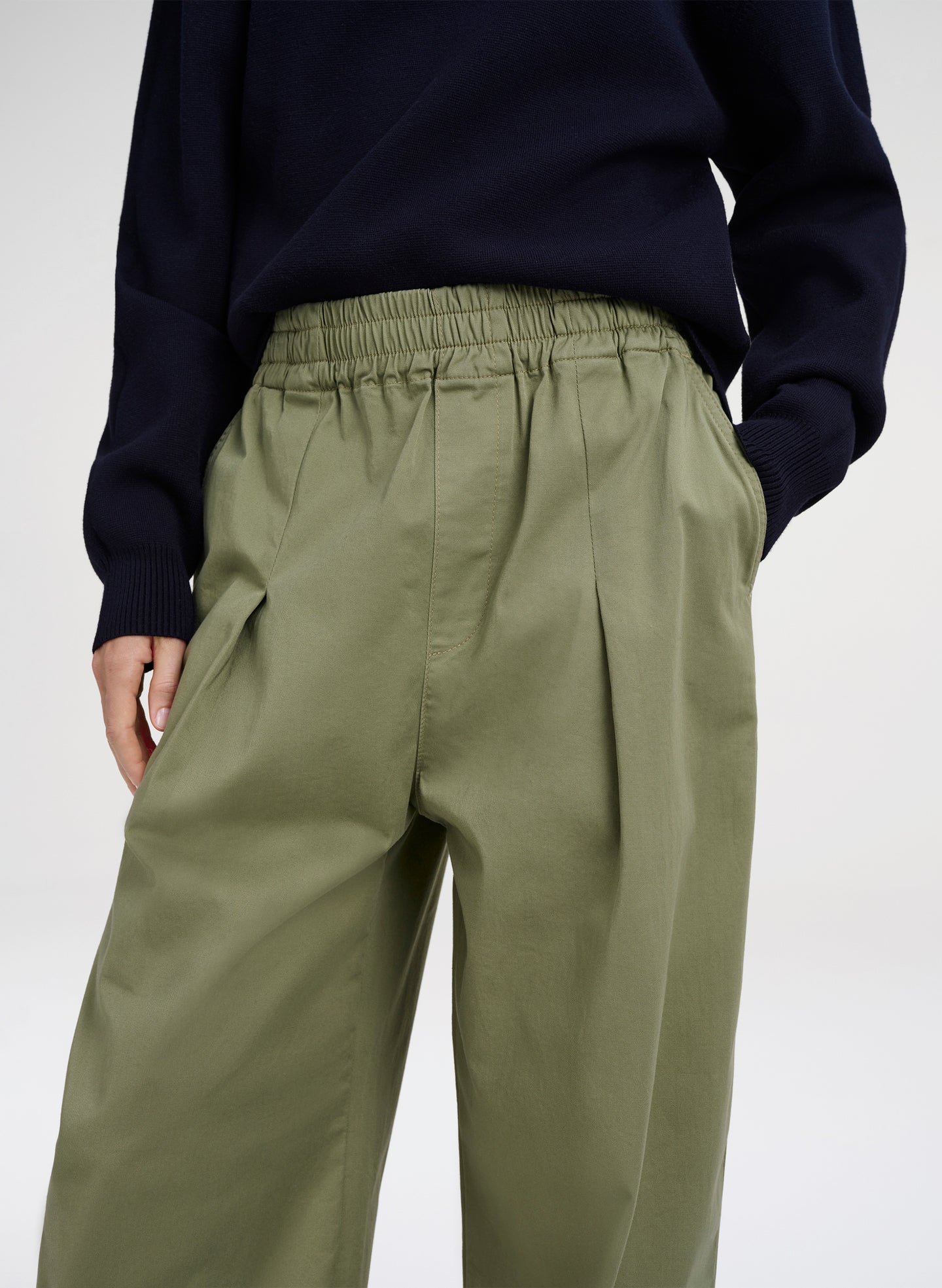 Person wearing olive green pants and a navy sweater on a white background
