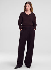 A woman modeling a dark brown v-neck knit sweater and matching dark brown wide-leg trousers against a light gray studio background.
