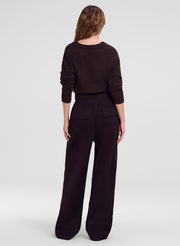 A woman viewed from the back wearing a brown knit sweater and matching wide-leg trousers against a light gray studio background.
