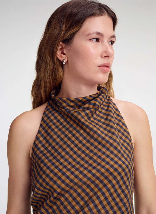 A woman wearing a sleeveless top with a brown and dark navy blue gingham check pattern, shown from the chest up against a light gray studio background.