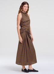 A woman modeling a sleeveless top and matching midi skirt with a brown and beige geometric pattern, styled with black slip-on shoes against a light gray studio background.