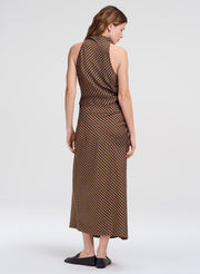 A woman shown from the back wearing a sleeveless brown outfit with a small repeating geometric pattern, photographed against a plain light gray studio background.