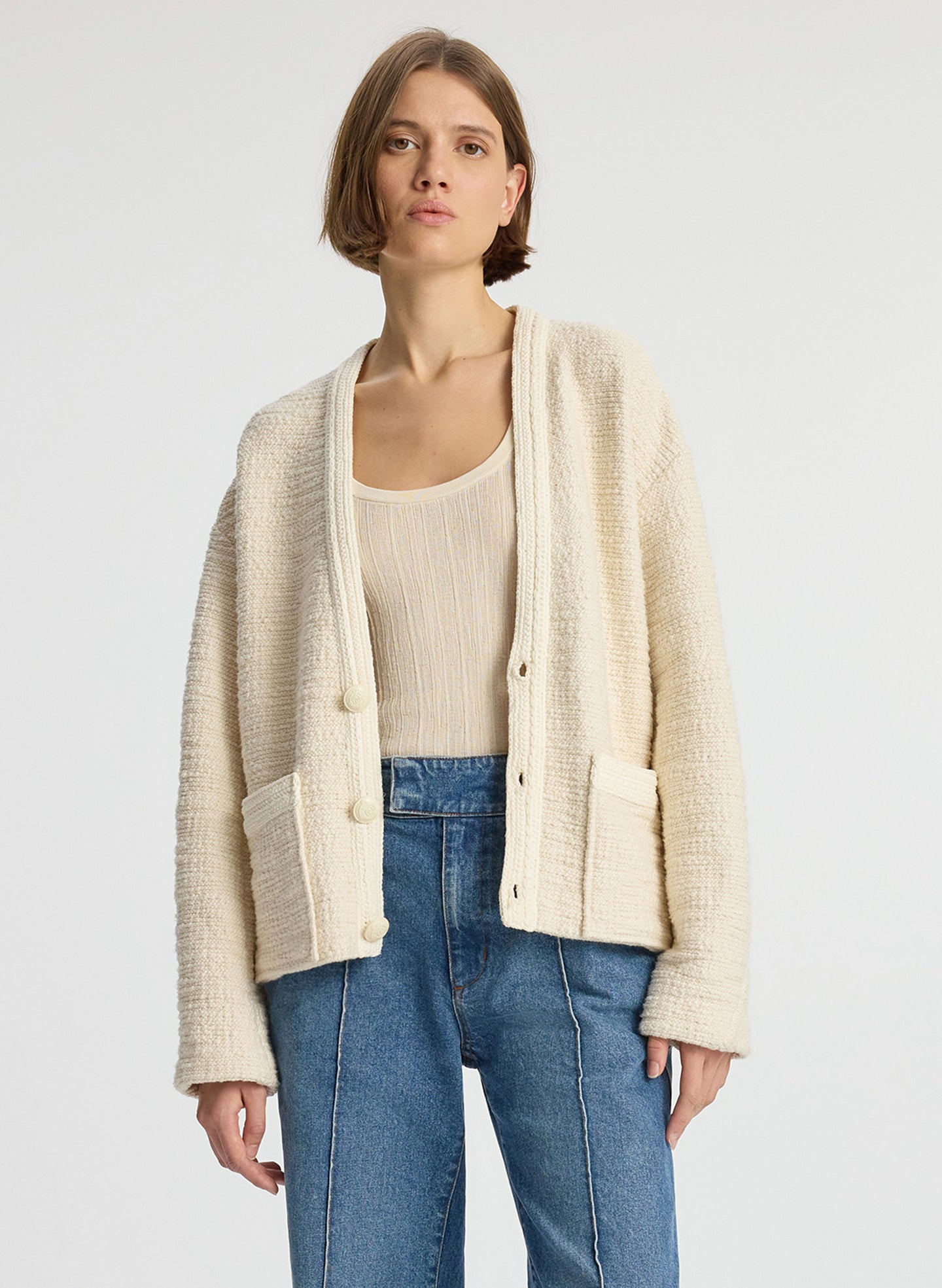 front view of woman wearing cream boucle jacket, cream tank top and medium blue denim jeans