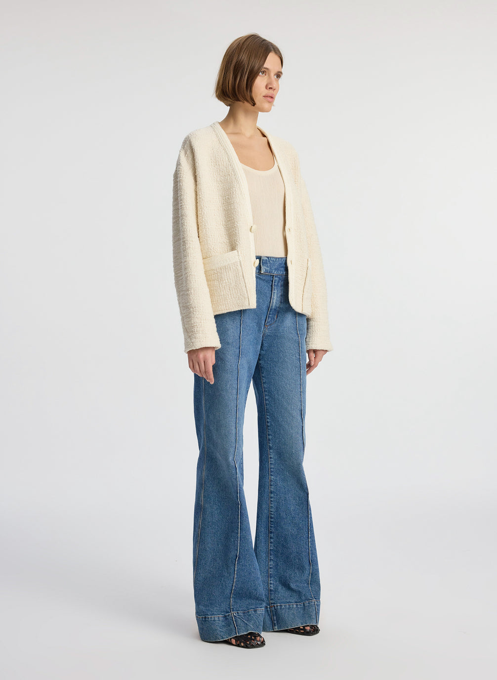 side view of woman wearing cream boucle jacket, cream tank top and medium blue denim jeans