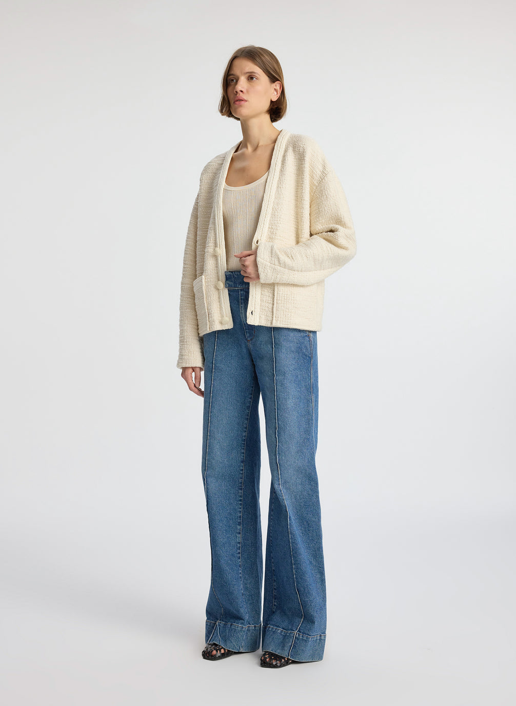 side view of woman wearing cream boucle jacket, cream tank top and medium blue denim jeans