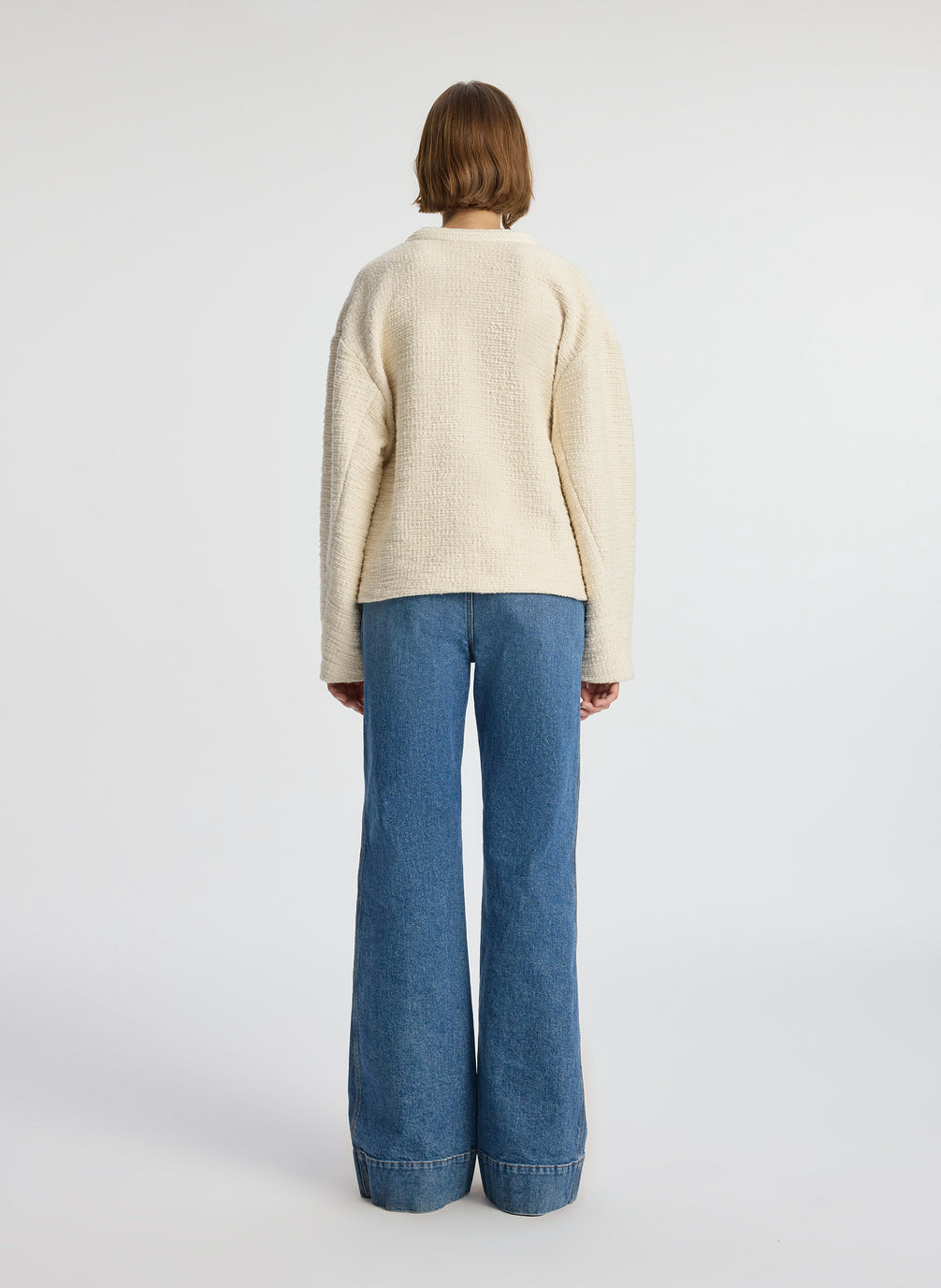 back view of woman wearing cream boucle jacket, cream tank top and medium blue denim jeans
