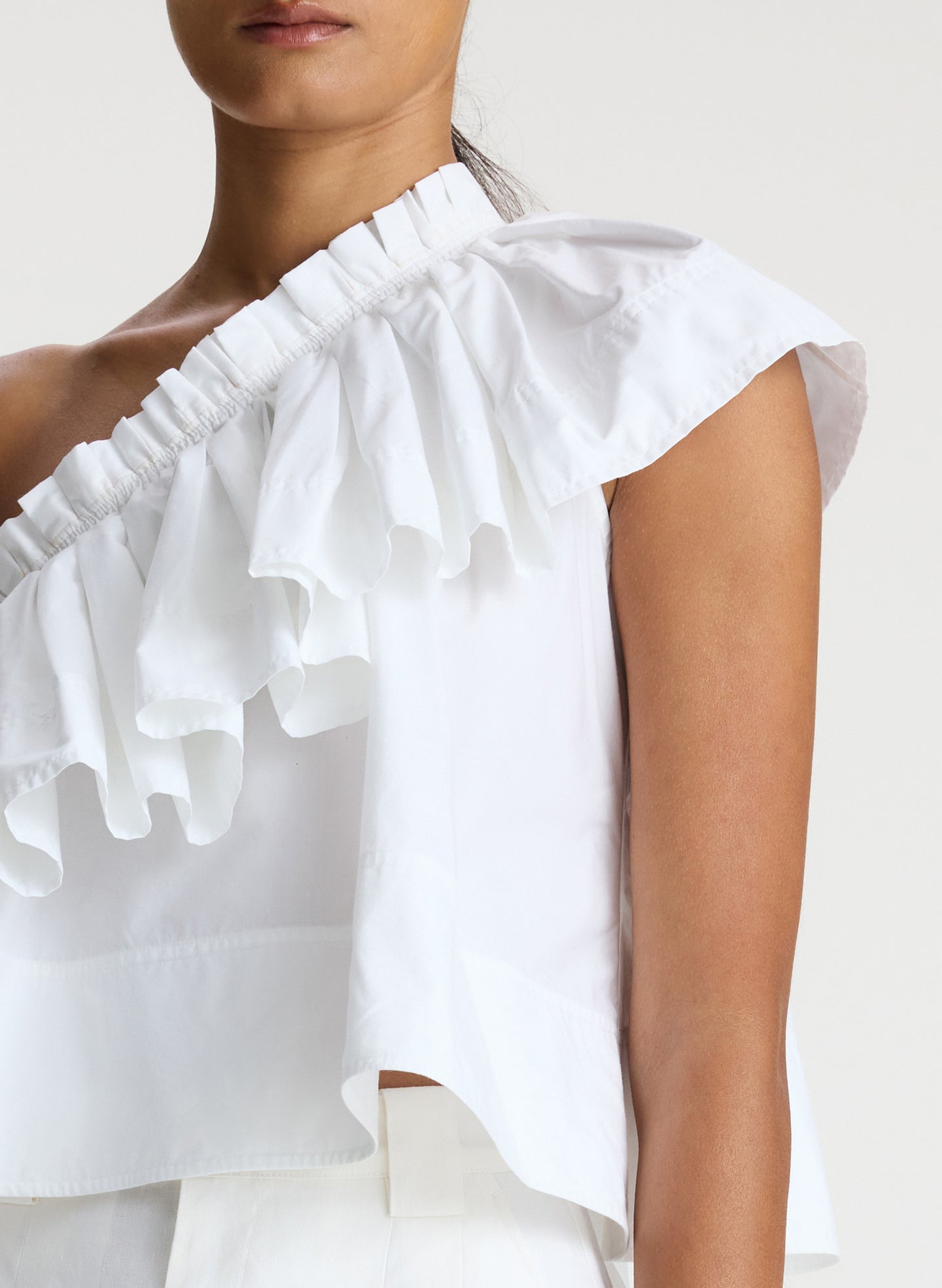 detail view of woman wearing white one shoulder ruffle top and white shorts