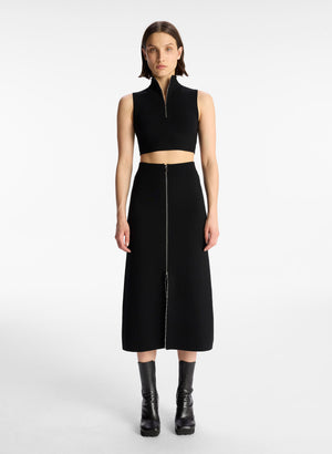front view of woman wearing black half zip sleeveless crop top and black midi skirt with contrast zipper