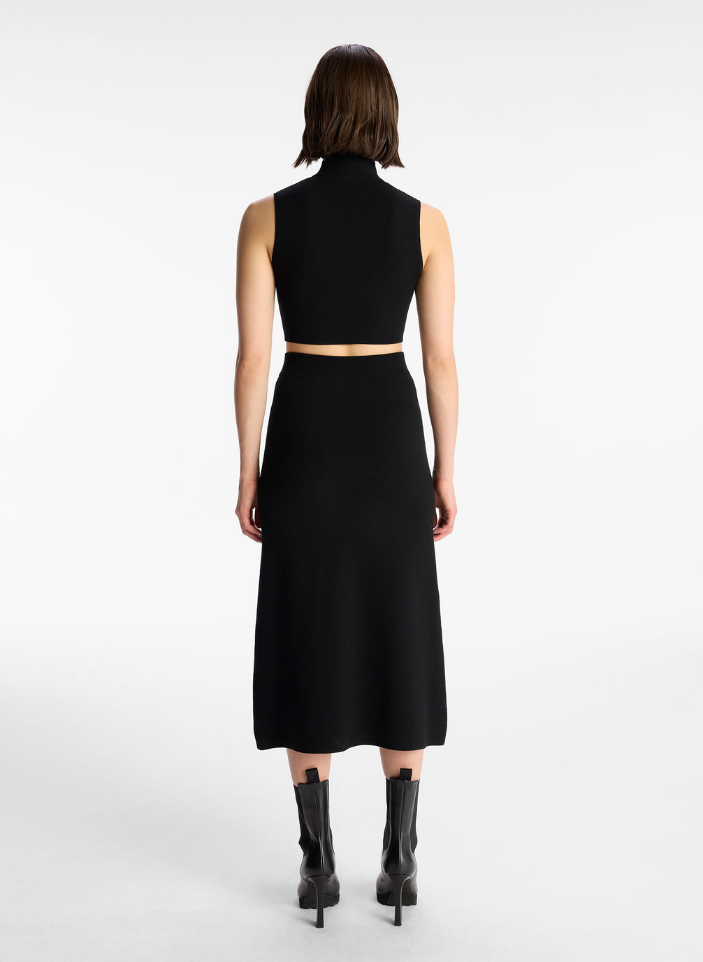 back view of woman wearing black half zip compact knit sleevless cropped top with matching black skirt
