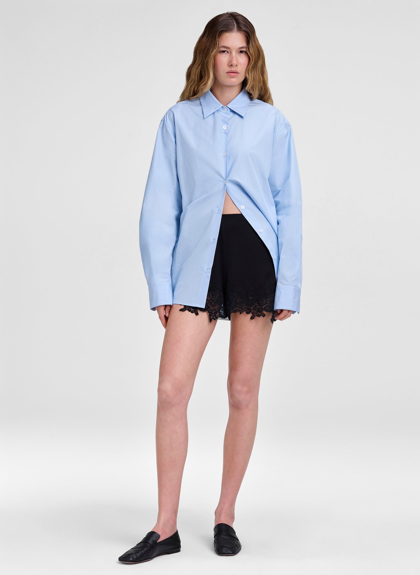 Person wearing a light blue shirt and black shorts on a white background