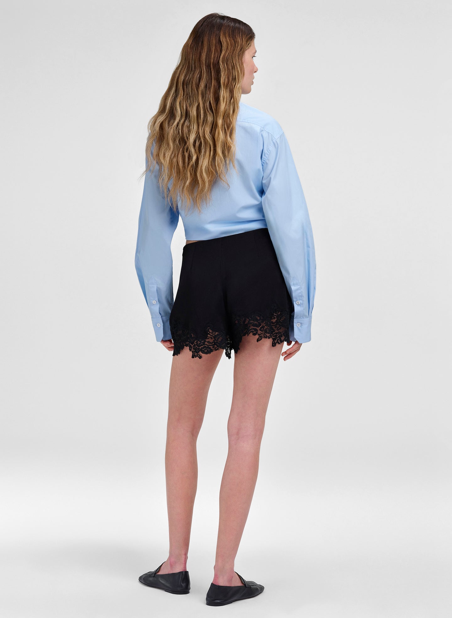 Person wearing a light blue blouse and black shorts with lace details on a white background