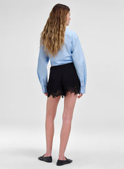 Person wearing a light blue blouse and black shorts with lace details on a white background