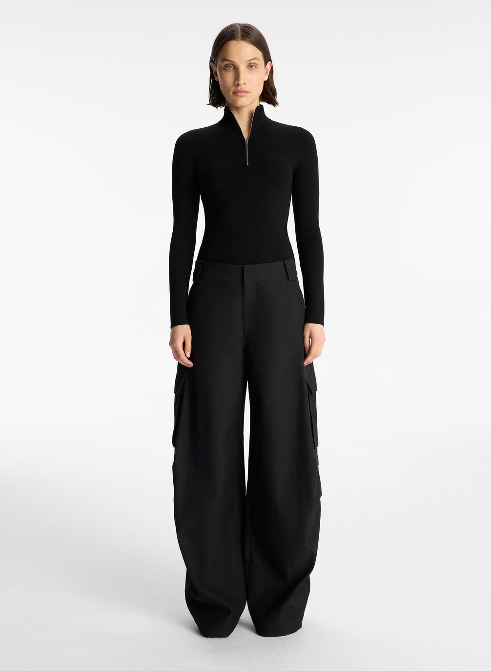 front view of woman wearing black half zip compact knit long sleeve top and black pants