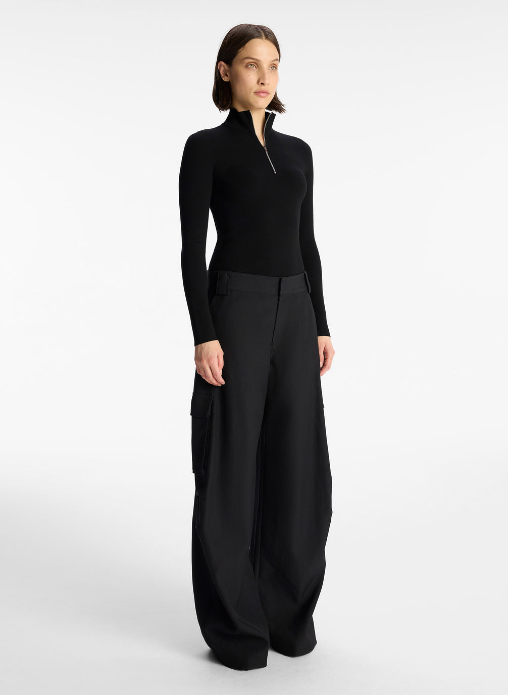 side view of woman wearing black half zip compact knit long sleeve top and black pants